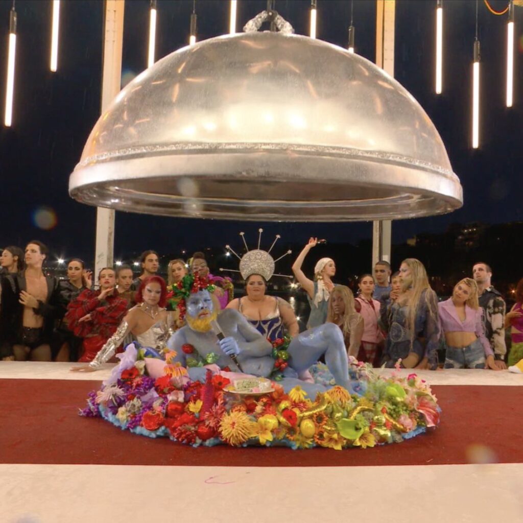 A still from the Paris 2024 Olympics Opening Ceremony featuring Philippe Katerine dressed as Bacchus, emerging from a banquet table in a grand artistic performance.